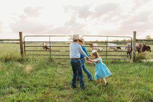 Dancing and spinning in a pastoral field next to metal farm gates at sunset.