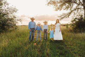 Family stands together in a grassy field at sunset wearing western attire and formal dress.