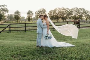 A romantic wedding couple shares intimate moments outdoors in a pastoral field with wooden fences and trees at sunset.