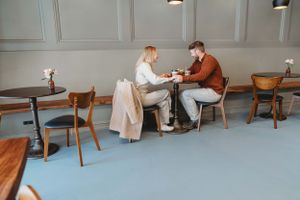 Two people share a meal together at a small table in a minimalist restaurant with blue floors and wooden chairs.