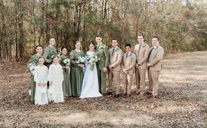 Wedding party poses together in neutral earth tones and light blue dresses against a wooded outdoor backdrop.