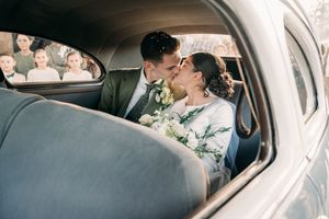 A couple shares an intimate moment while sitting in a car during a wedding celebration.