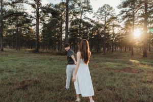 Couple walks hand in hand through pine forest at golden sunset.