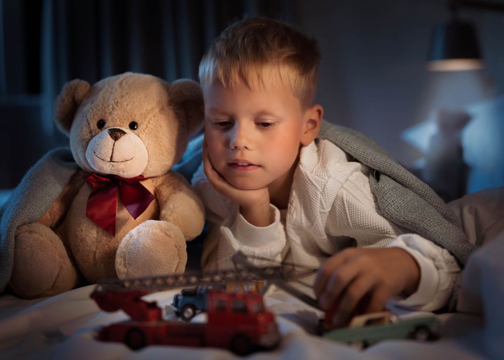 Child relaxing in bed with a teddy bear and toy car in soft evening lighting.