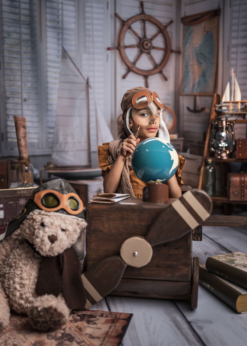 Vintage aviation-themed room with teddy bear, ship wheel, globe and wooden toy plane decor.