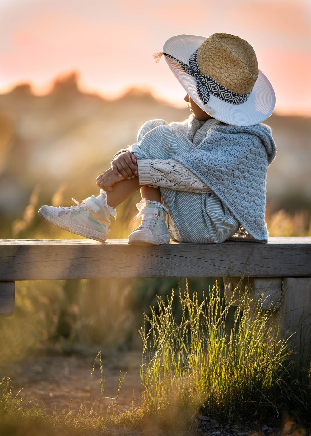 A peaceful sunset scene with someone wearing a straw hat sitting on a wooden bench.