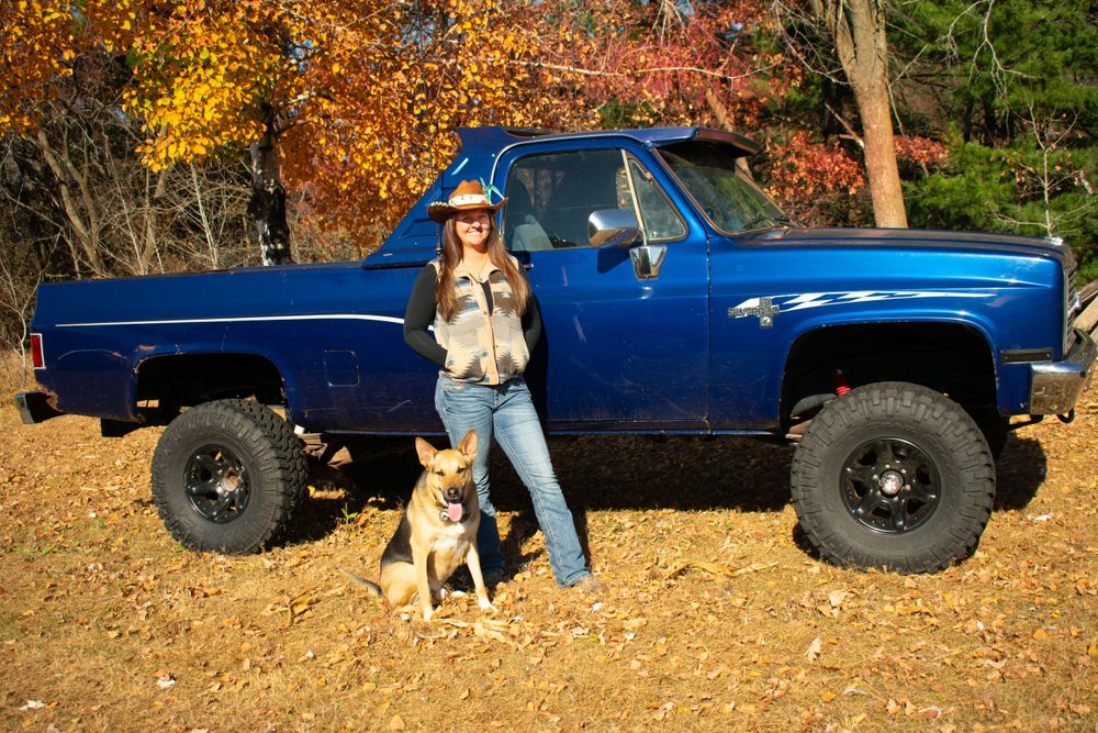 Woman and her dog in front of a 1984 blue square body chevy.