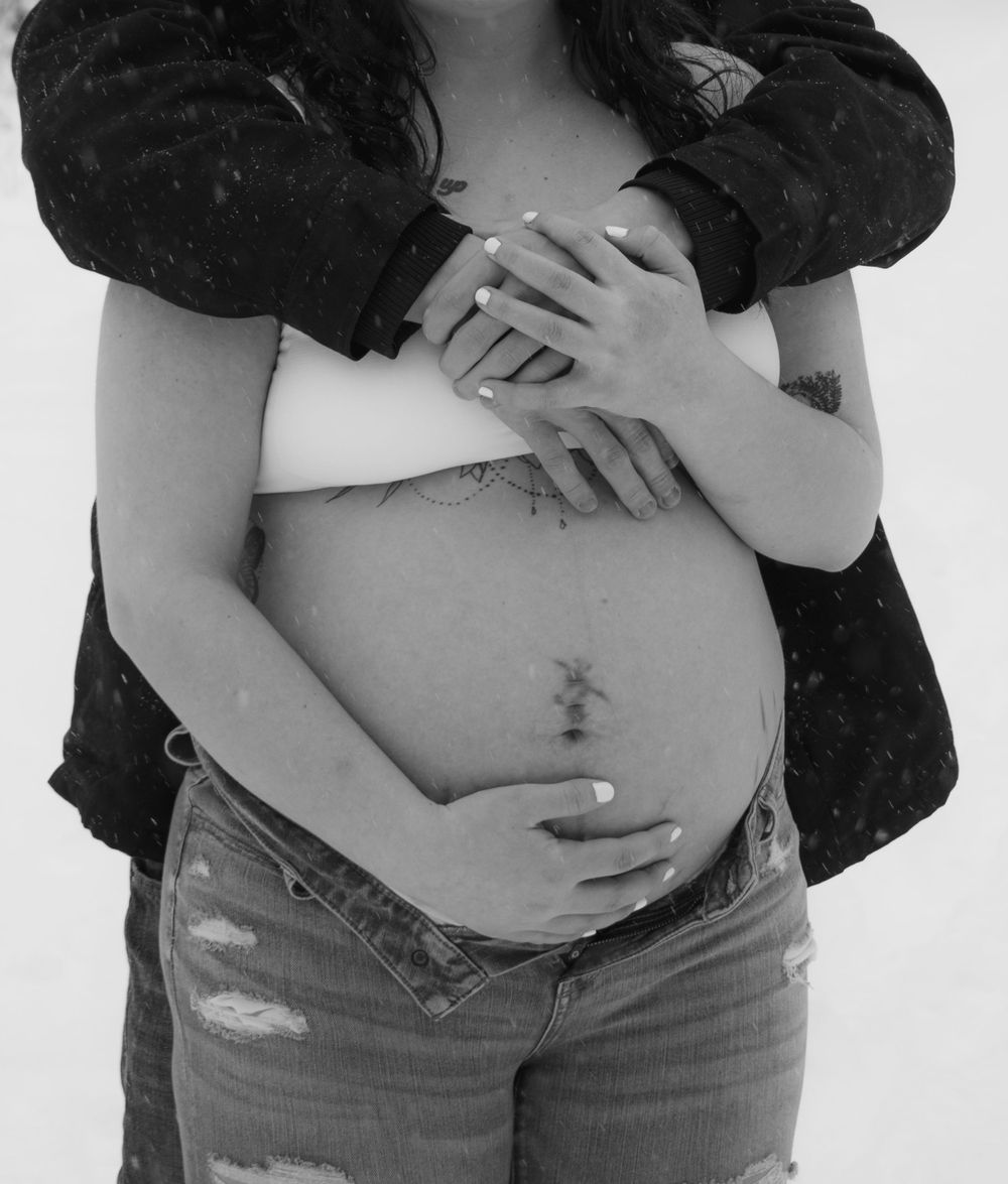 Black and white photo of pregnant mother to be and partner focusing on the baby belly in a Wisconsin woodsy winter scene