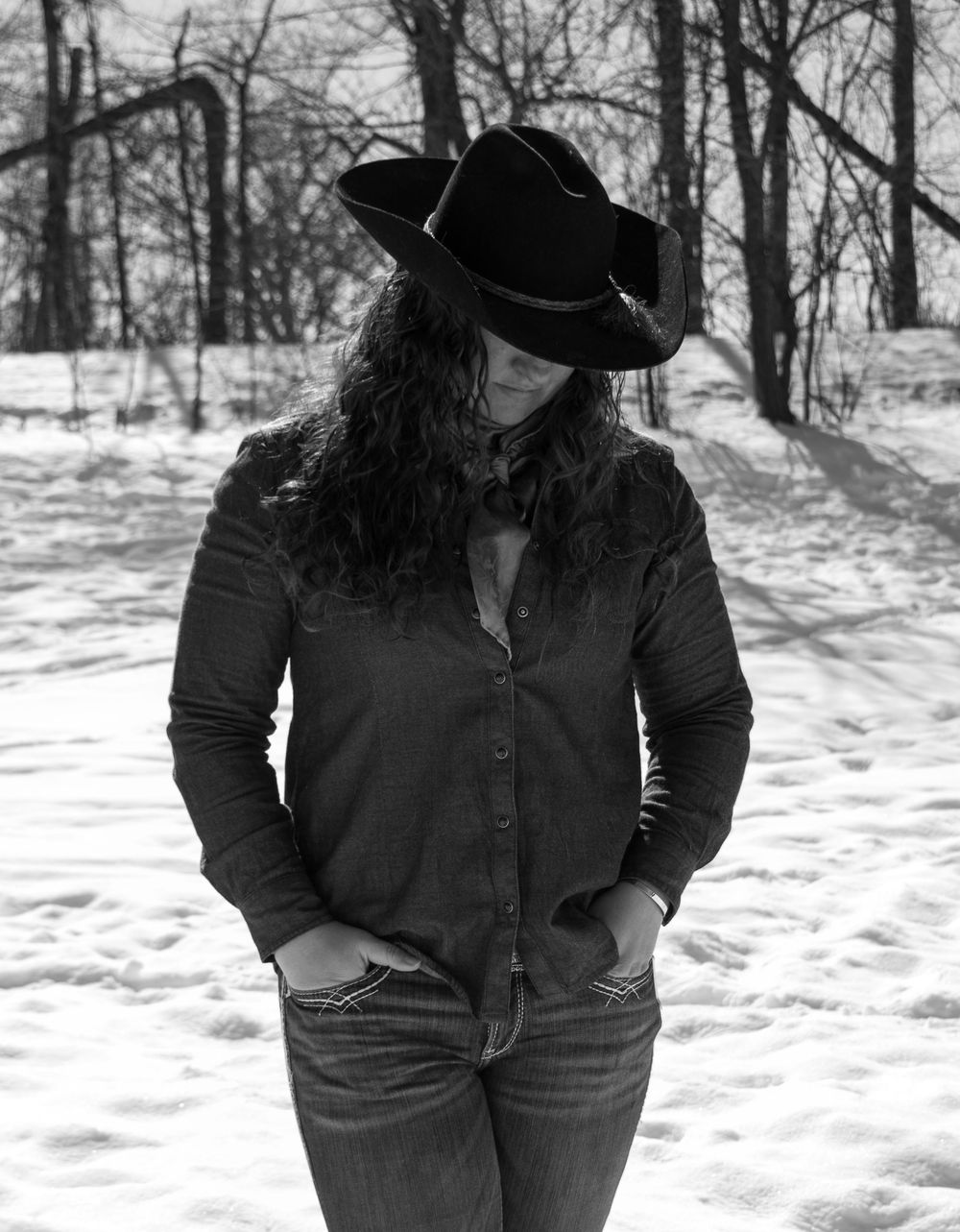 Black and white photo of cowgirl standing with hands in pocket, looking down in a Wisconsin winter scene