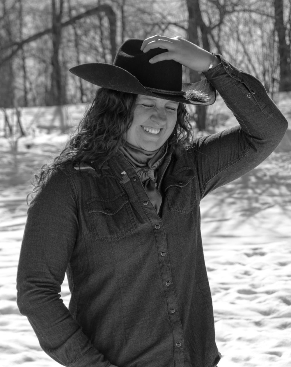 Cowgirl with hand on hat, laughing in a Wisconsin winter scene