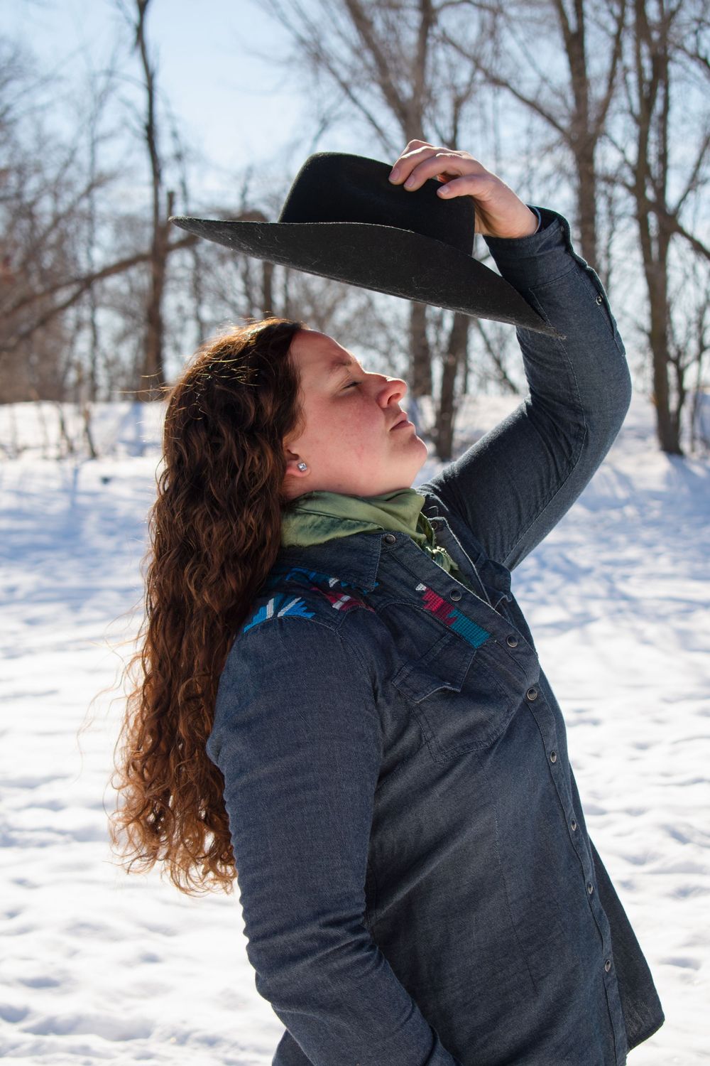 Cowgirl standing with hat over head, eyes closed in a Wisconsin winter scene