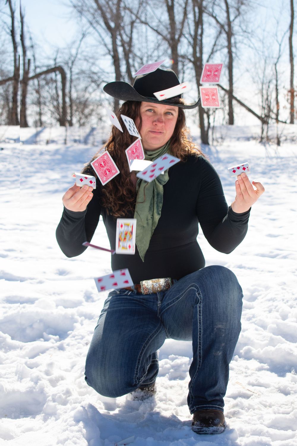 Cowgirl kneeling down, with playing cards in the air, framing her face in a Wisconsin winter scene