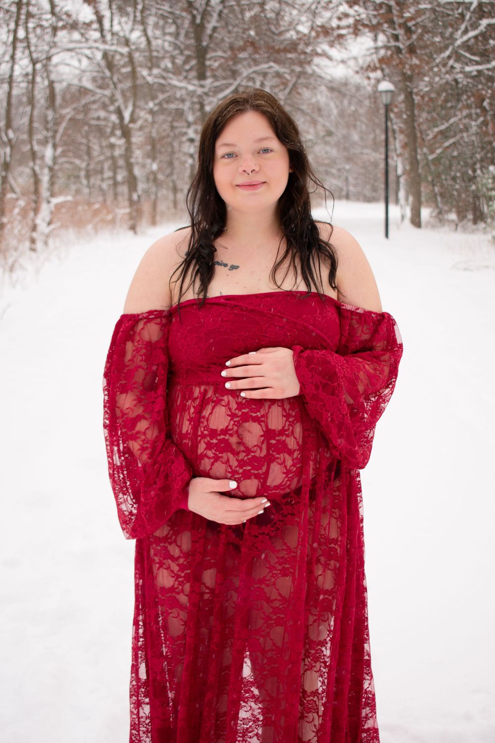 Pregnant mother to be looking at camera with hands on belly in a Wisconsin woodsy snowy scene