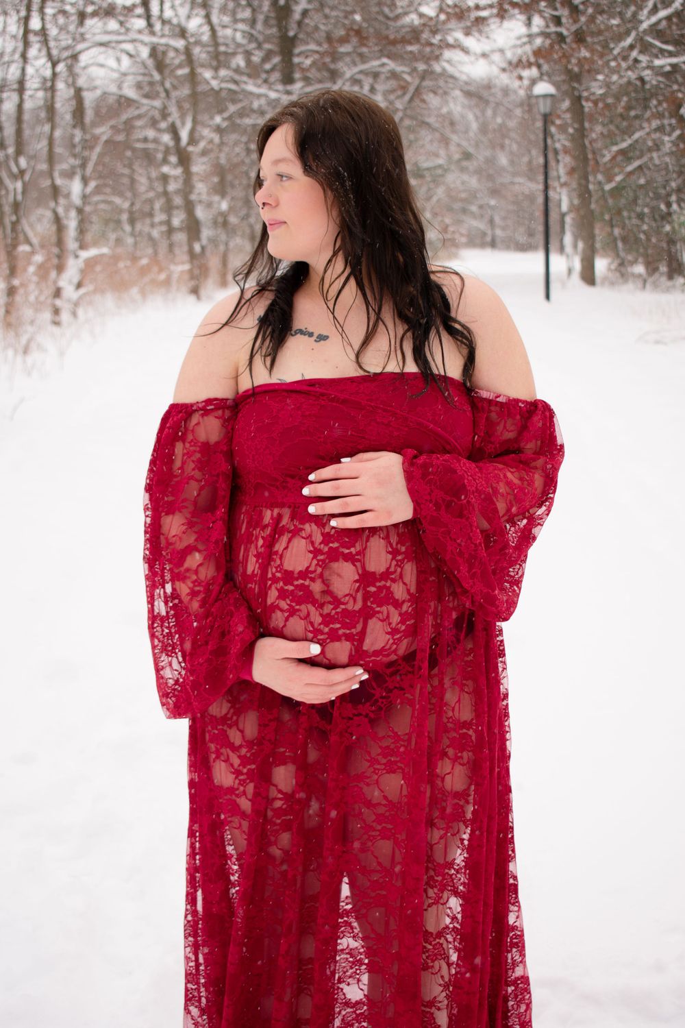 Pregnant mother to be looking off to side with hands on belly in a Wisconsin woodsy winter scene