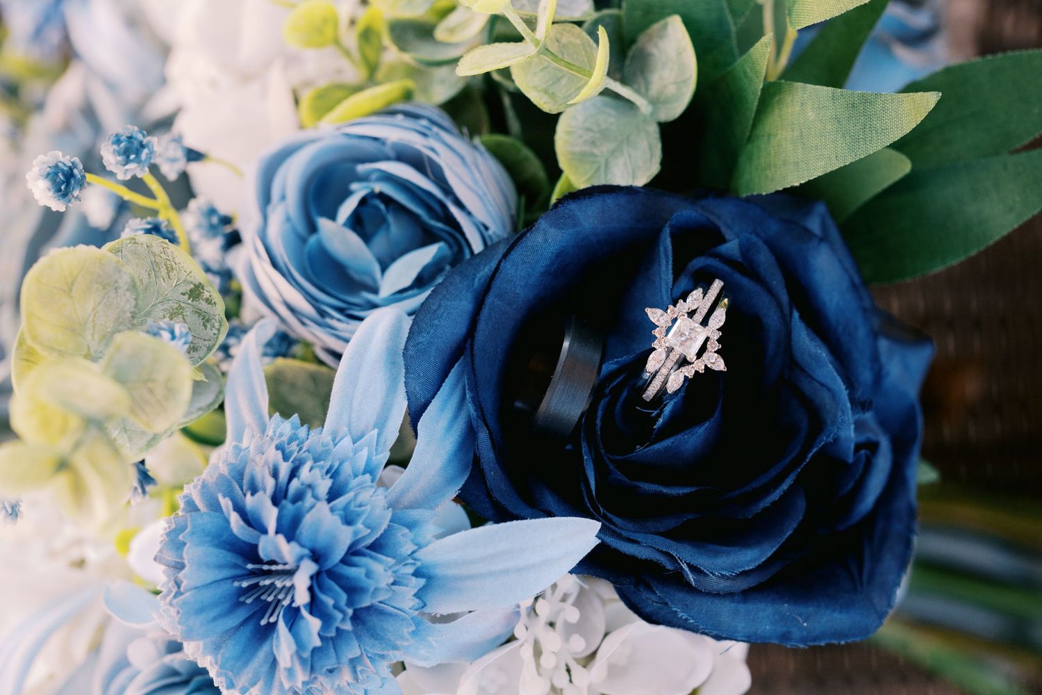 Close up of bridal bouquet featuring navy blue and light blue silk flowers with sparkling diamond engagement ring.