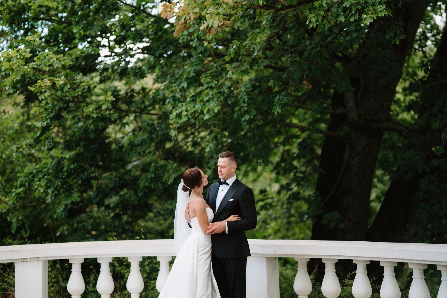 Wedding ceremony taking place on an elegant white railing deck surrounded by greenery.