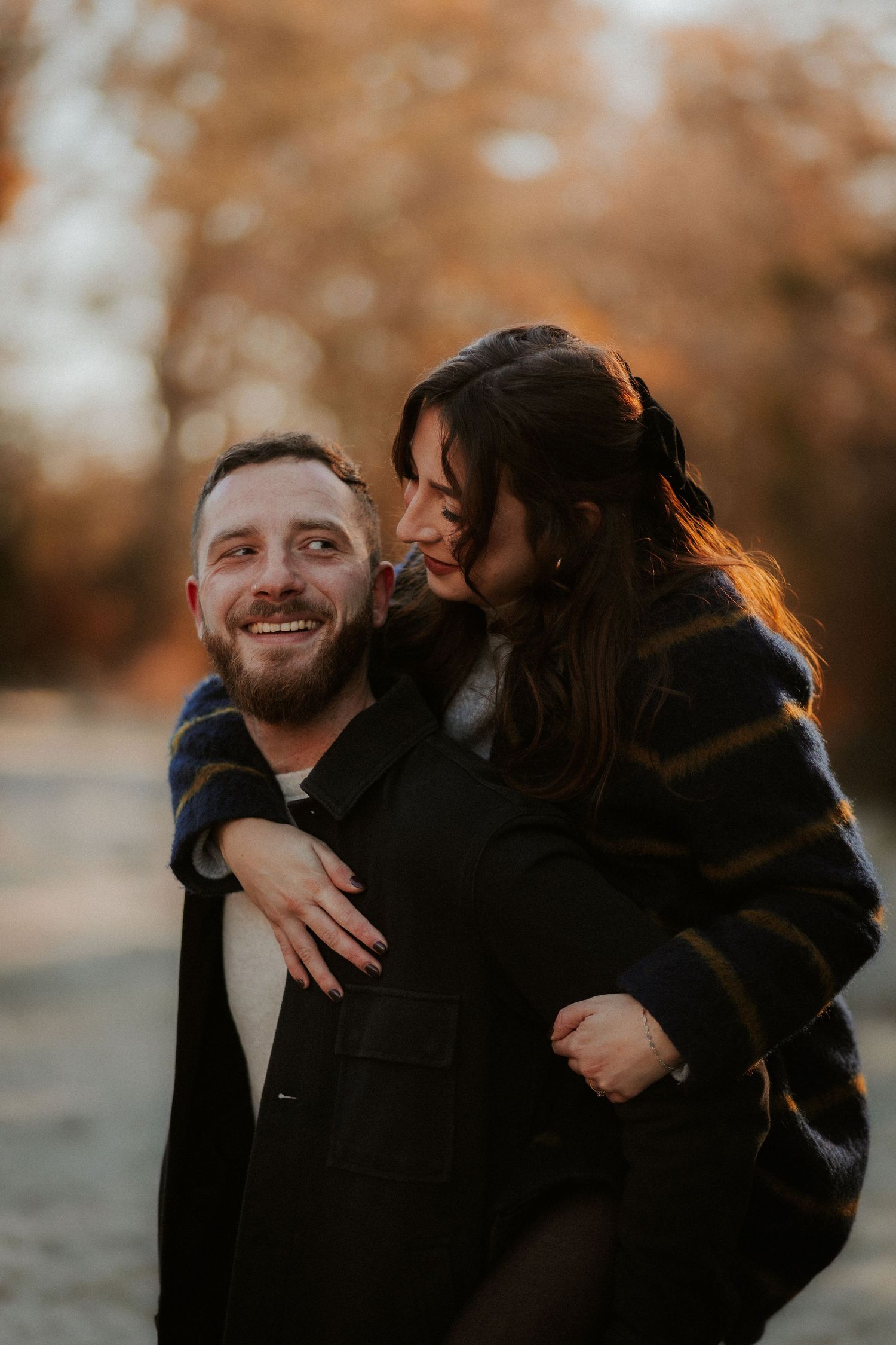 A playful autumn photoshoot of a couple sharing a piggyback ride in golden evening light.