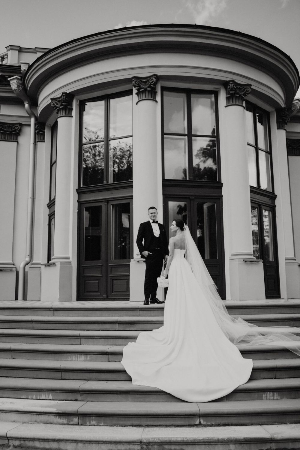 Black and white architectural photo of a couple on grand steps with curved windows.