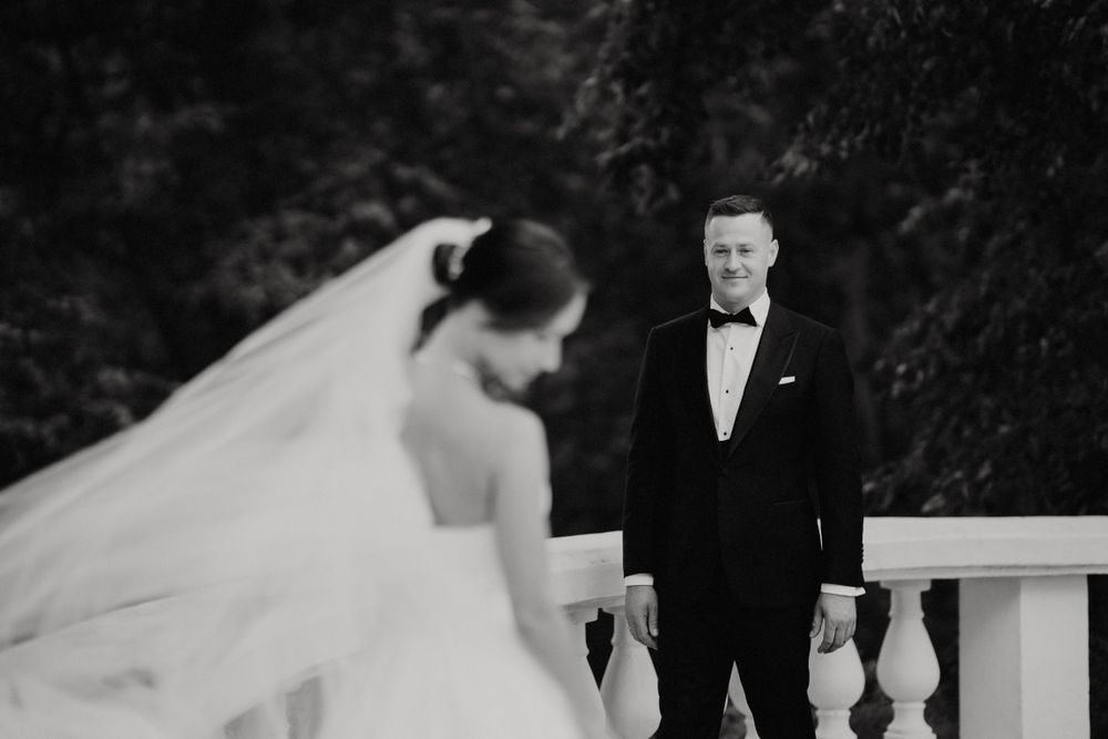 A black and white wedding photo captures a romantic moment on a classic stone balustrade.