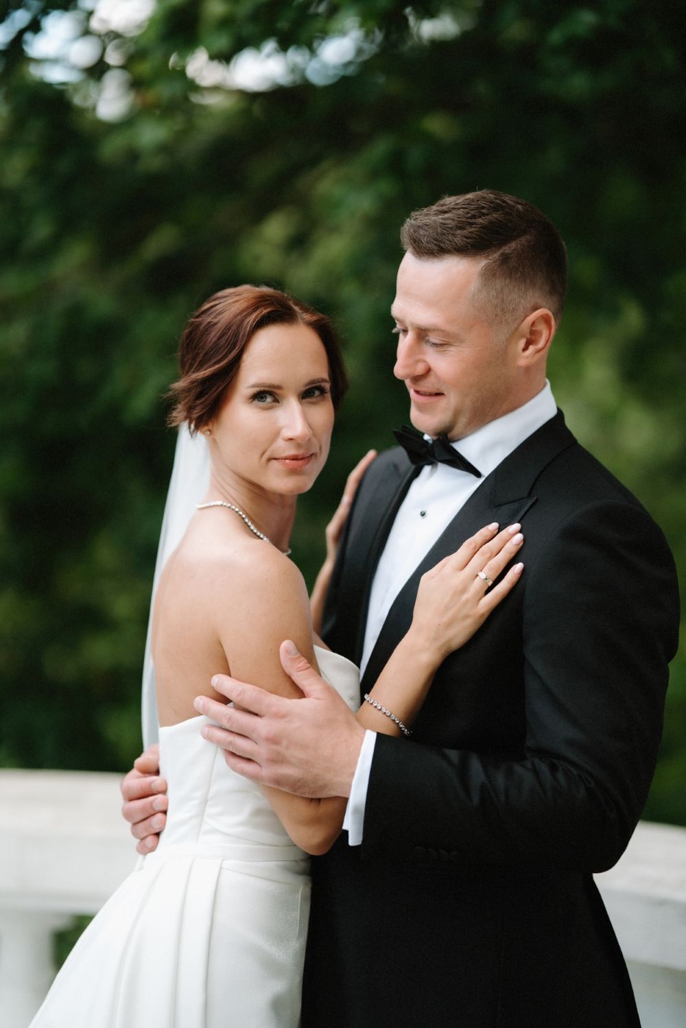 A tender moment between newlyweds in formal attire against a white balustrade.