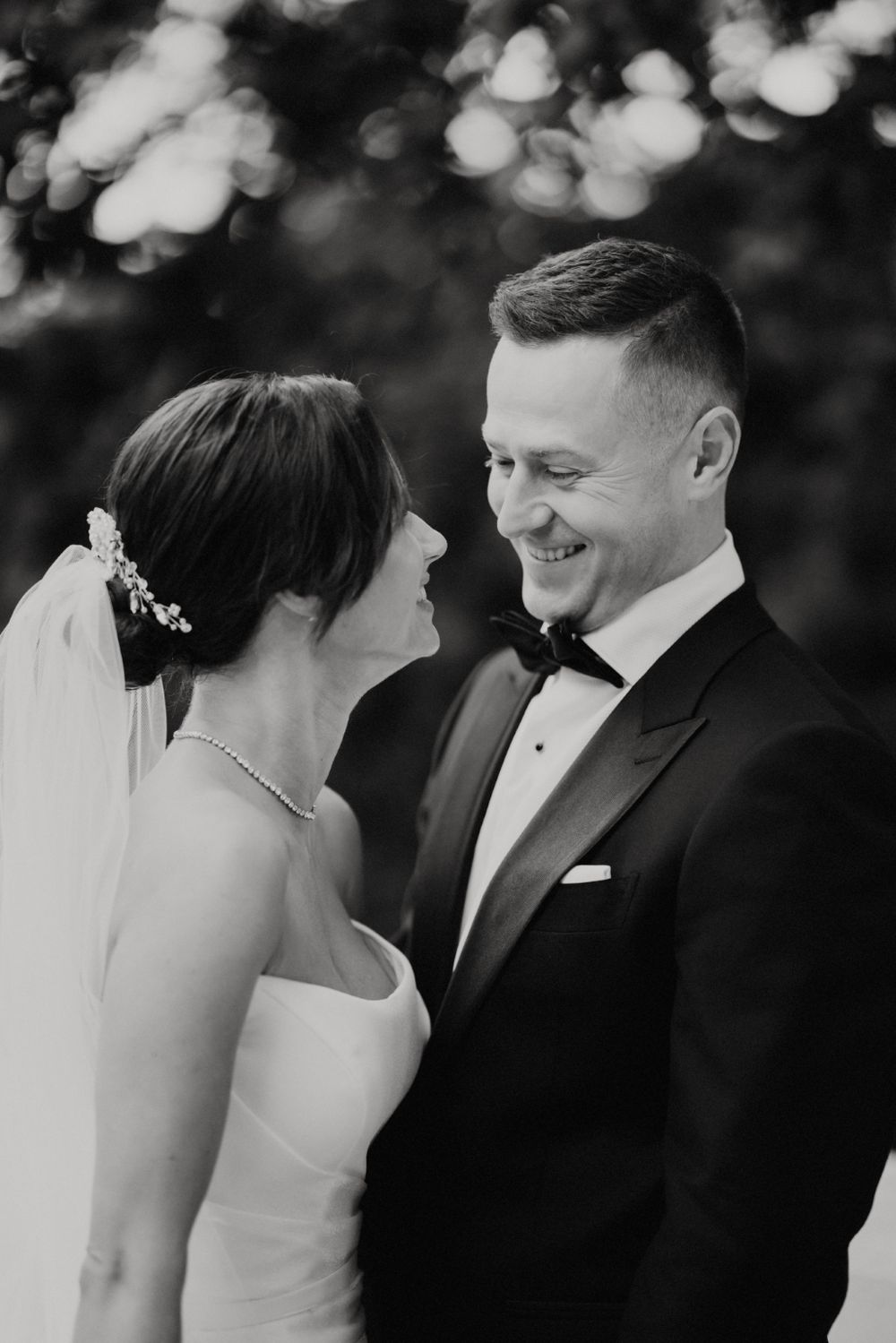 A black and white portrait captures an intimate wedding moment with soft bokeh lighting.