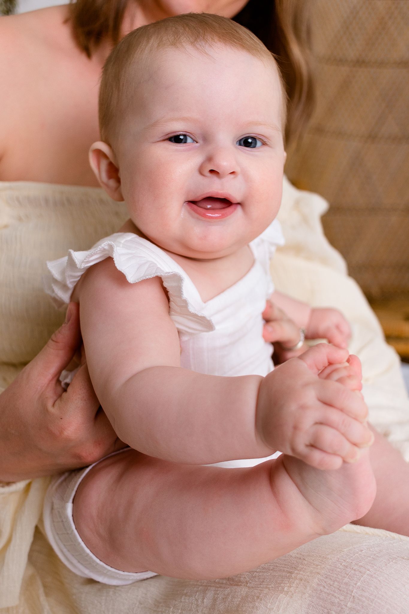 six month old girl sitting and holding her toes while sitting on her moms lap