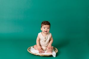 six month old boy sitting on wicker round with green backdrop in background