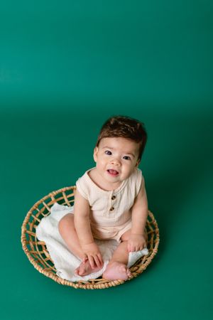 six month old boy sits on wicker circle with green background