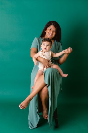 mother sitting on stool in front of green background with six month old son in her lap