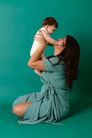 mother holding son up in the air both looking into each others face. son holds mothers face in hands
