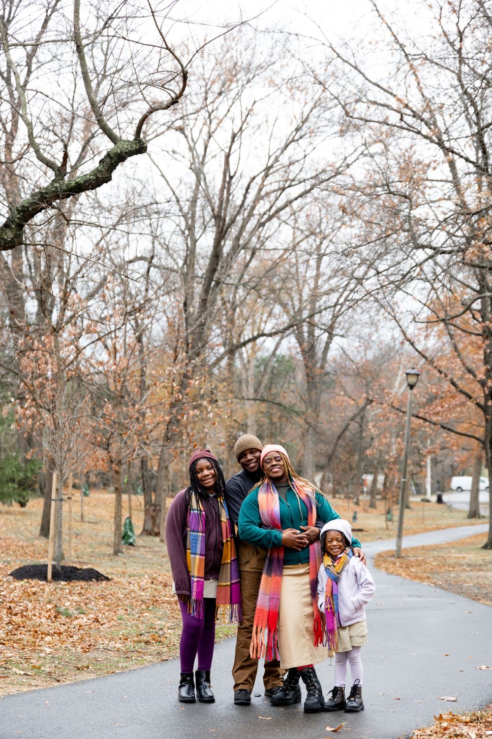 A group walks together on a paved path through a park on an autumn day with fallen leaves scattered around.