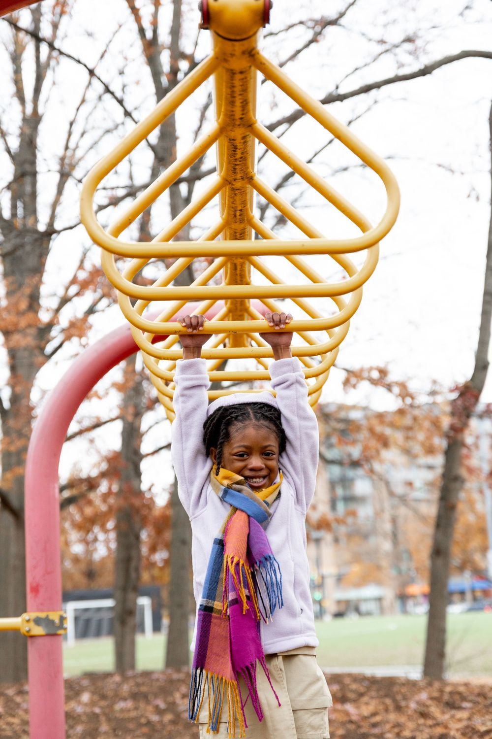 A child plays on yellow playground equipment in a park during fall season while wearing a colorful scarf.