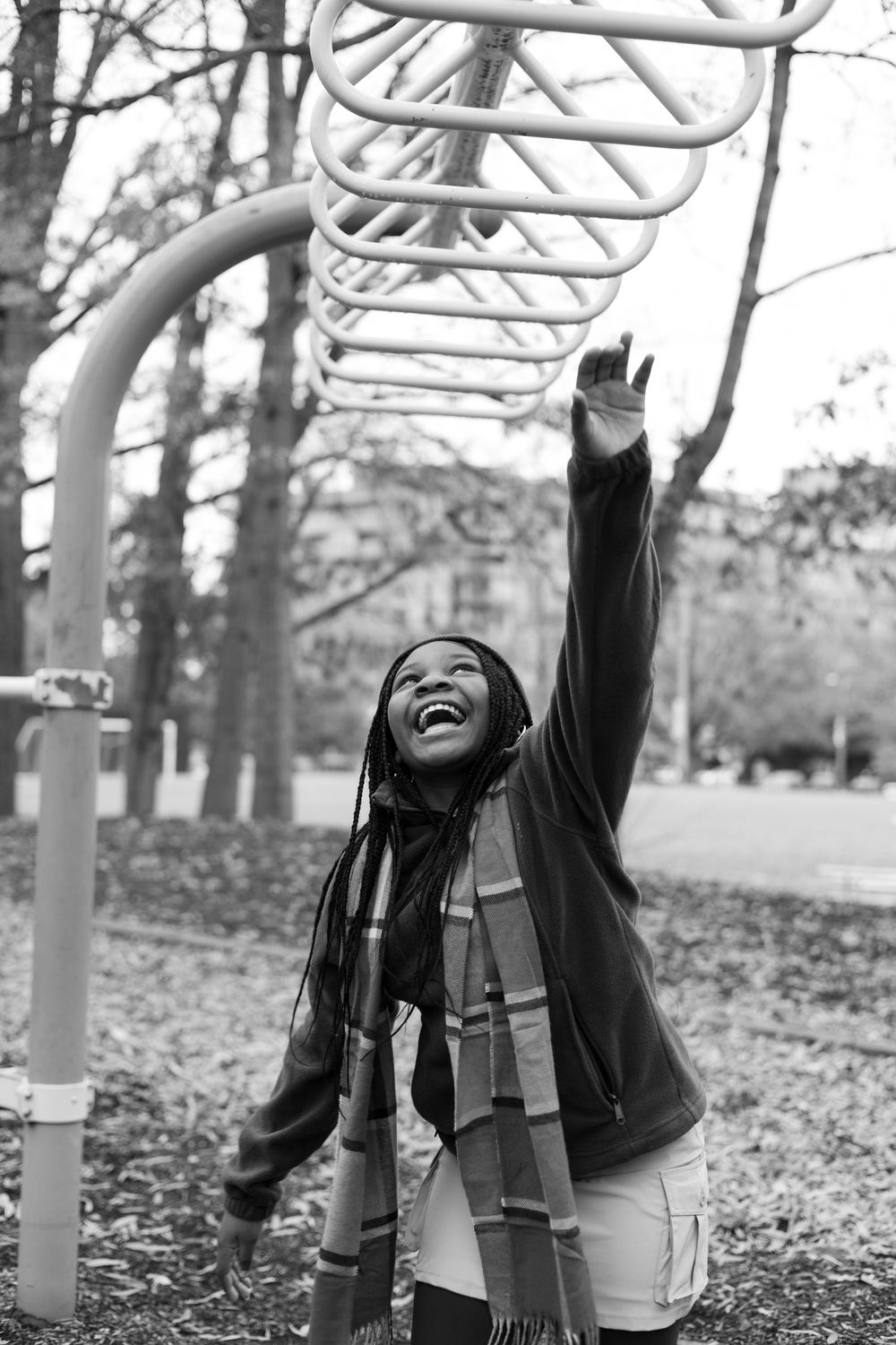 A sequence of four black and white photos showing someone joyfully playing on monkey bars in a park during autumn.