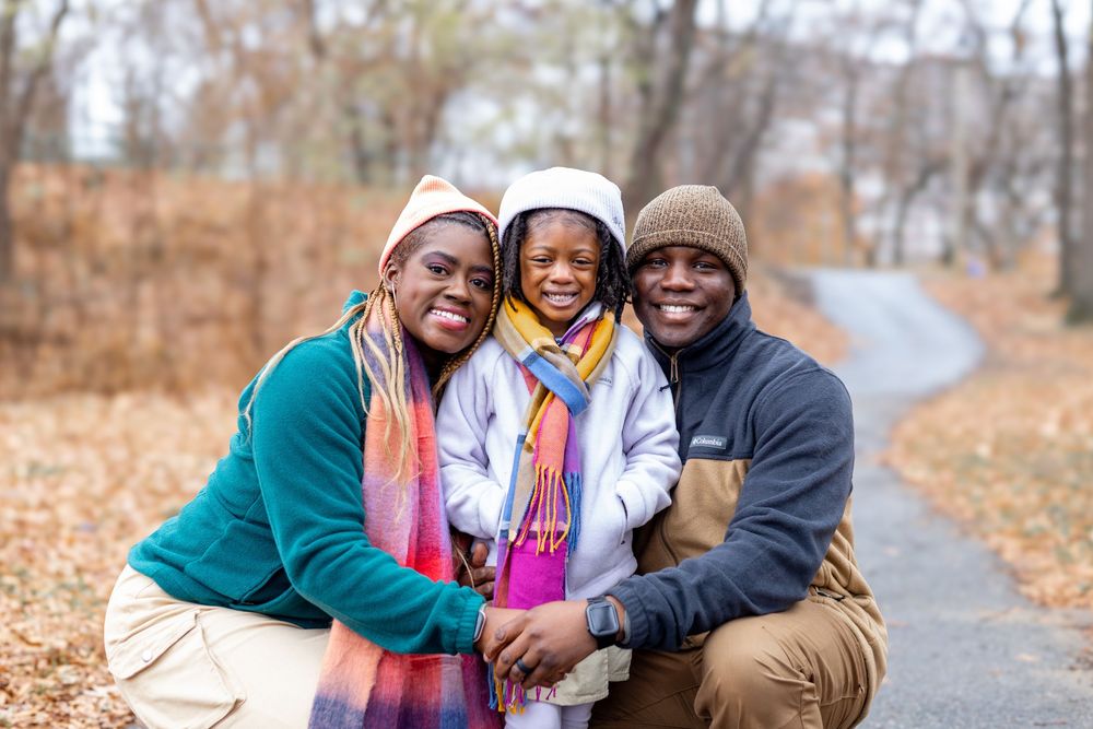 Family enjoying a playful autumn photoshoot together on a leaf-covered path in the woods.