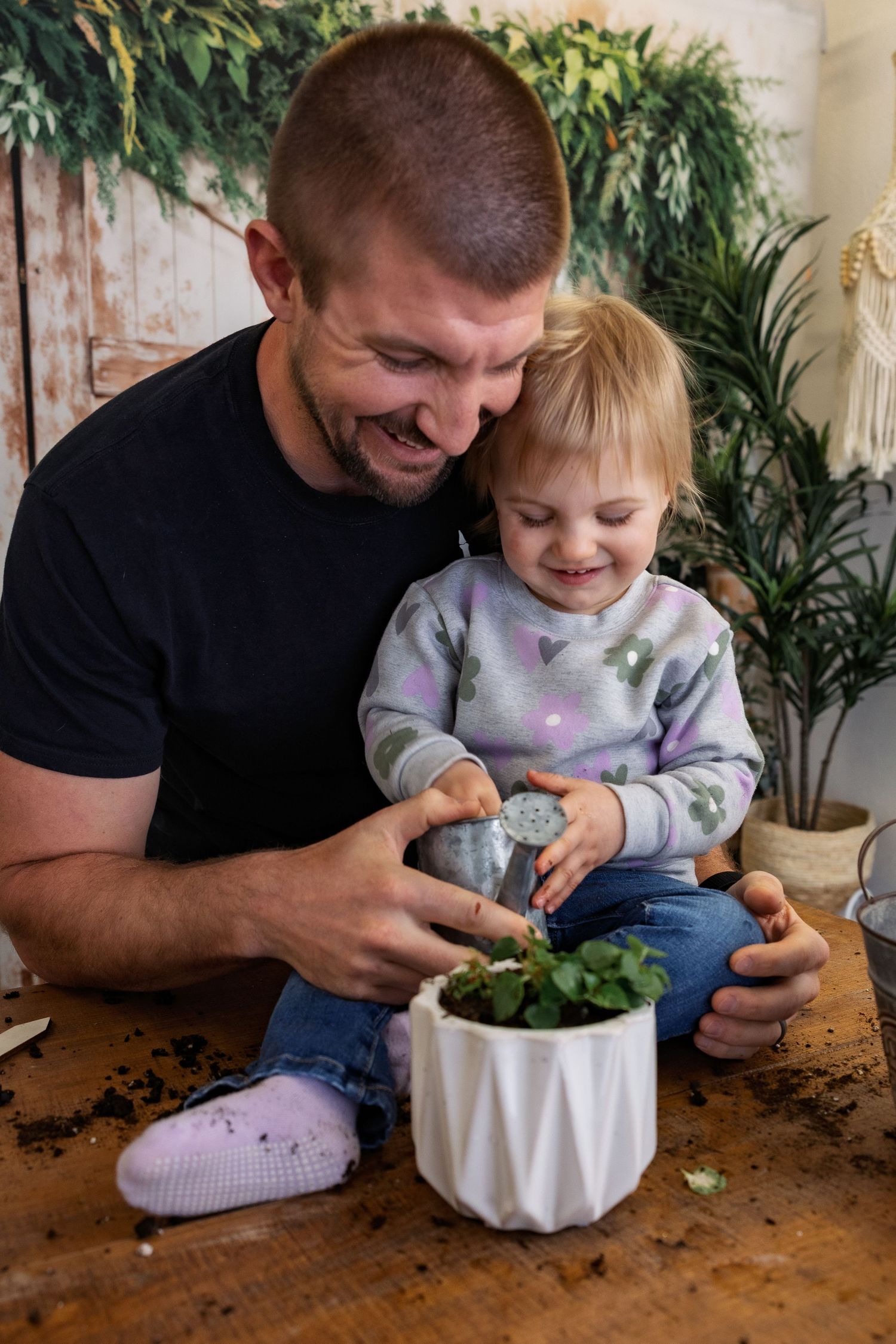 A heartwarming moment of a dad and his daughter planting a small plant in a white geometric planter on a wooden table during a mini shoot.