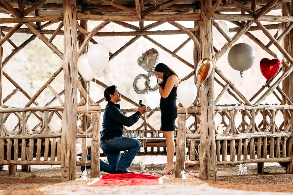 People enjoying a rustic wooden pavilion decorated with red hearts and white balloons for a romantic celebration.