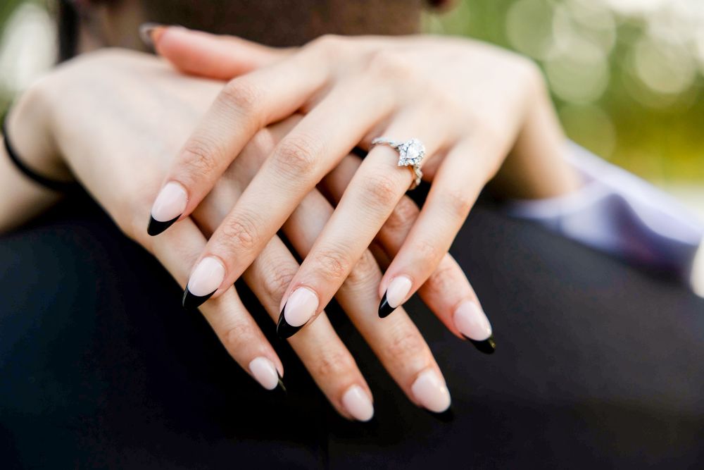 Close-up of manicured hands with French tips showing off an engagement ring with bokeh background.