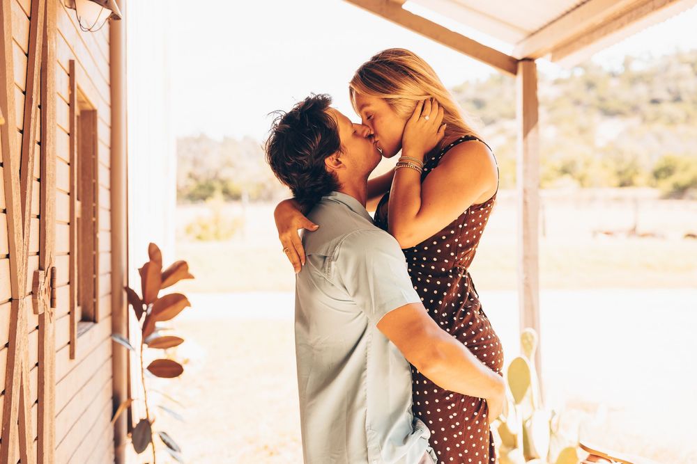 Romantic couple embraces on rustic porch with desert landscape in background during golden hour sunset.