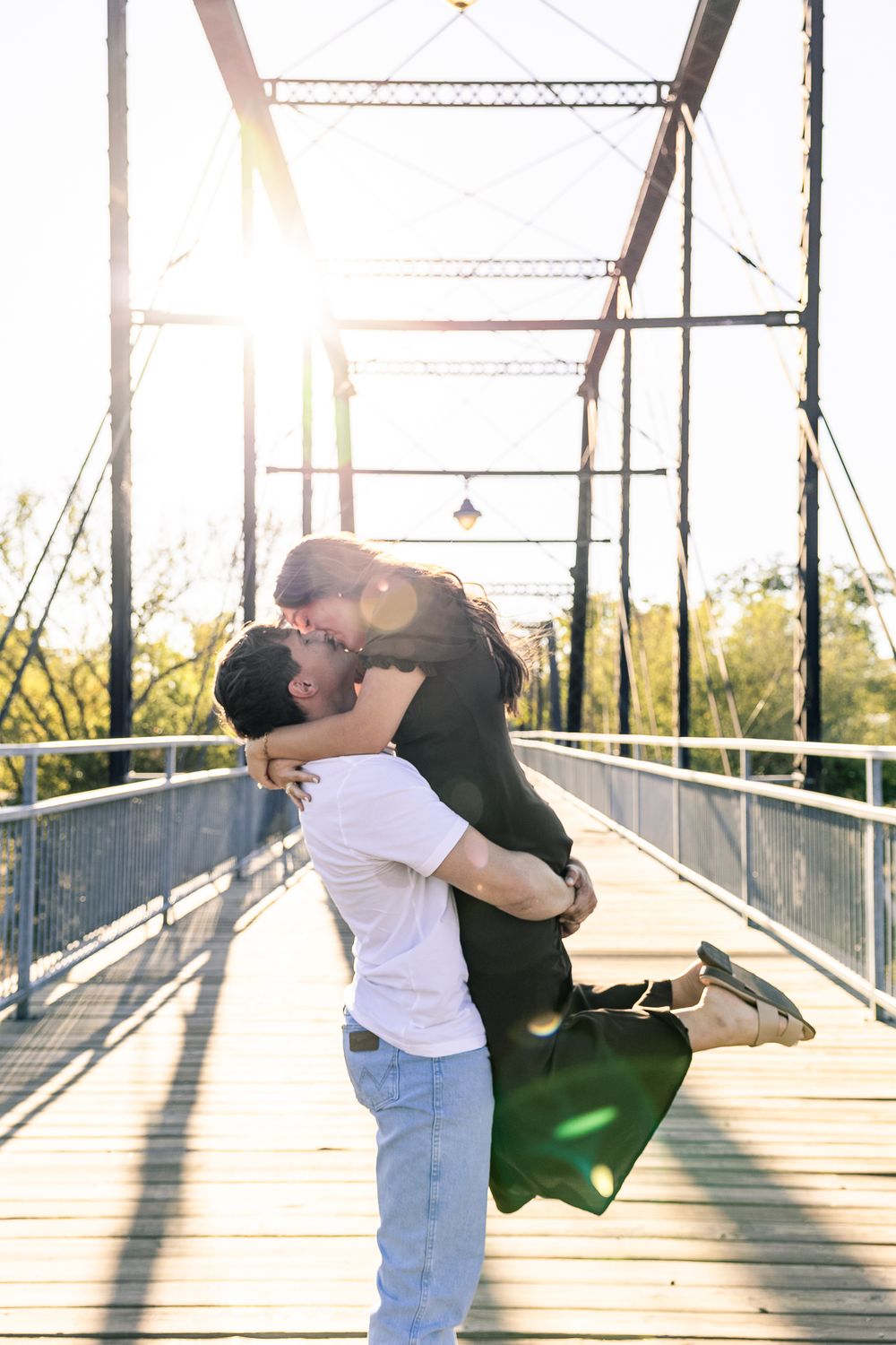 Two people embrace and dance together on a sunlit wooden bridge, creating a romantic silhouette against the railing.