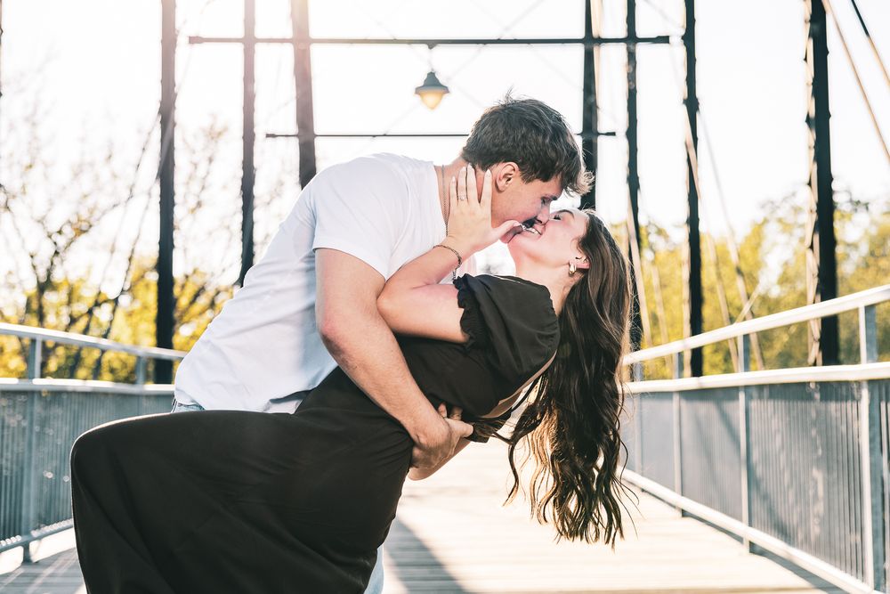 A couple embraces on a contemporary bridge with metal railings during sunset.