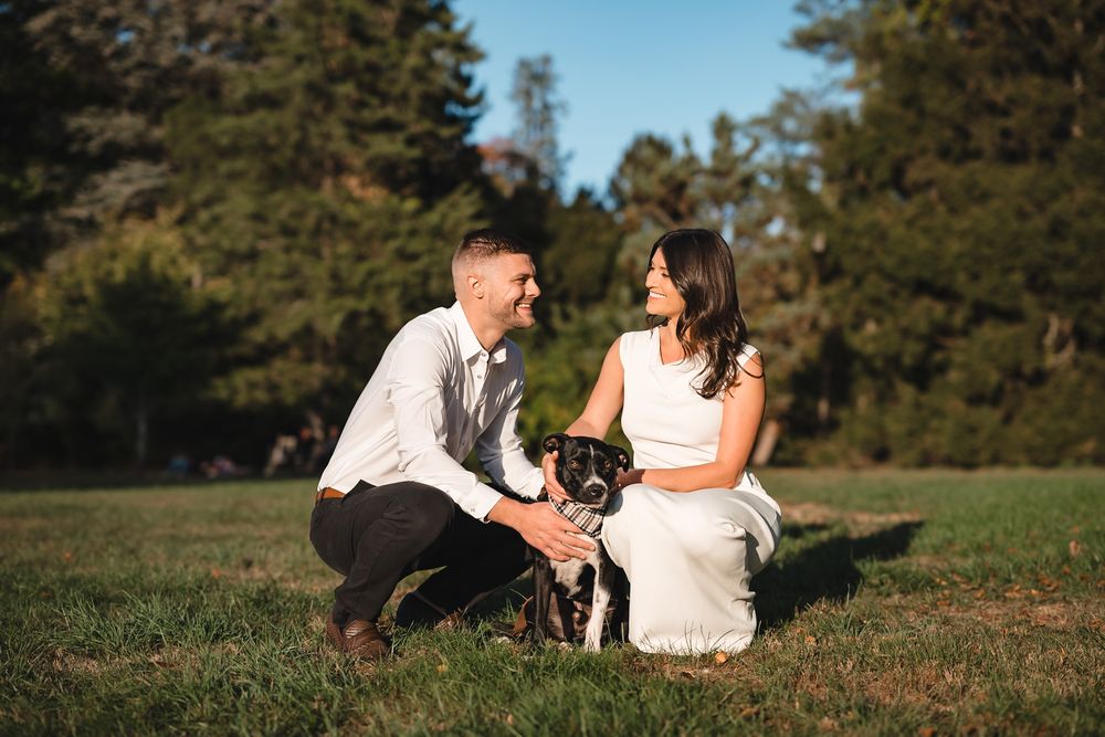 Couple relaxes on grassy hill during outdoor photo session at sunset.