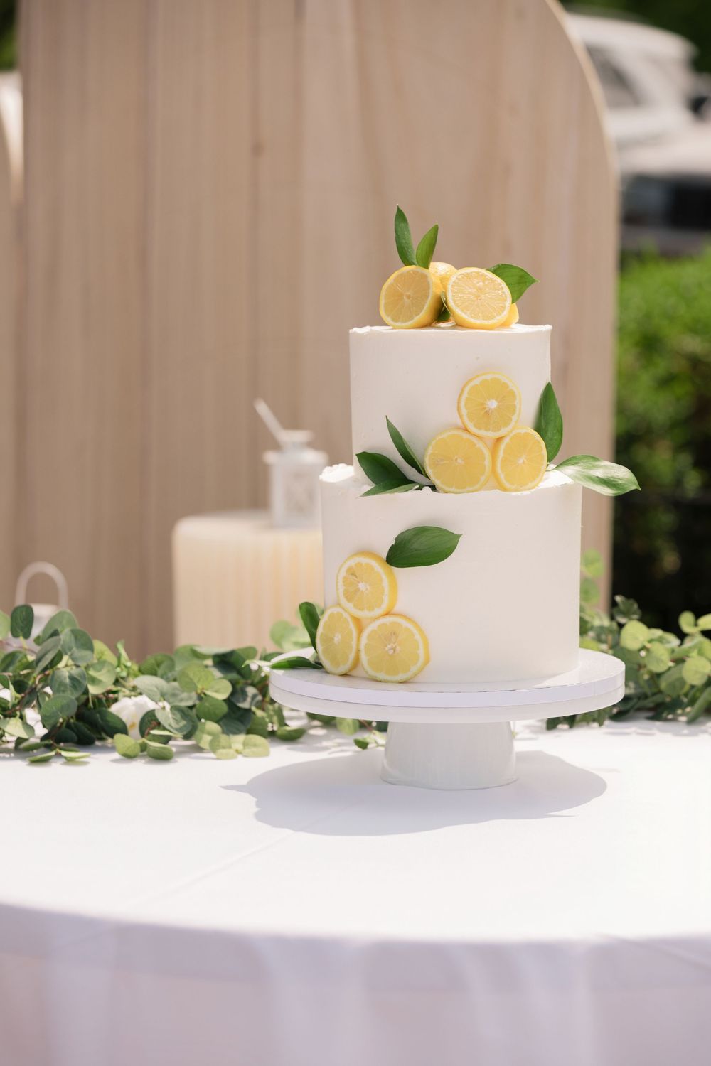White tiered wedding cake decorated with fresh lemon slices and green leaves on a white stand.