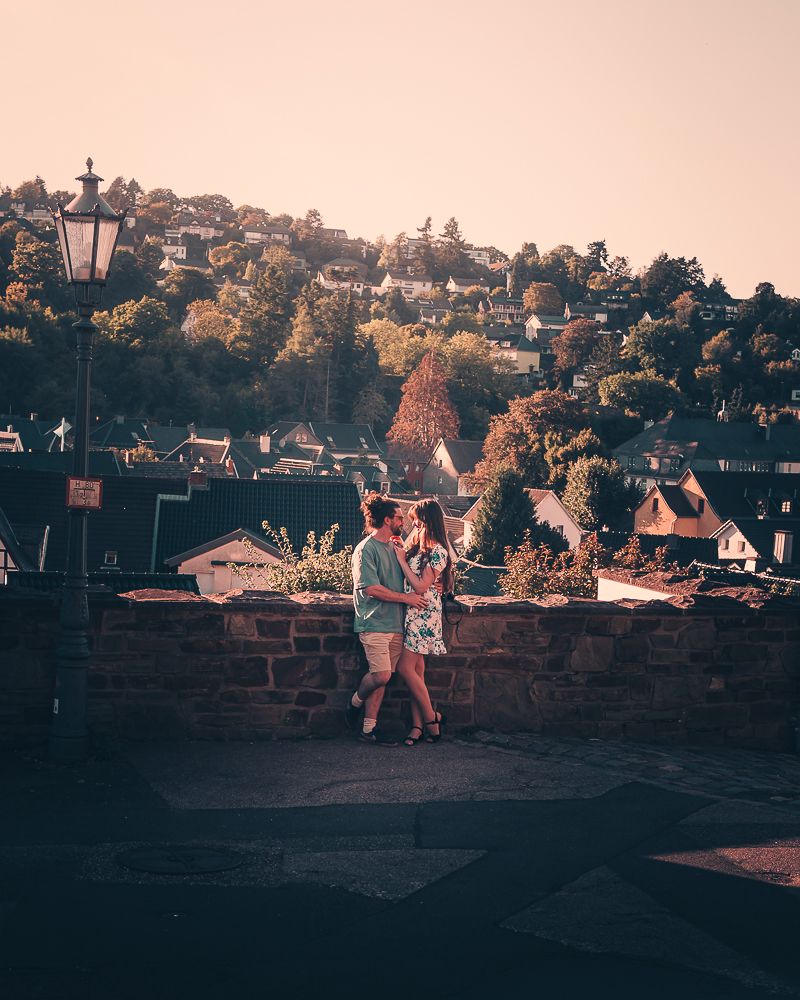A couple shares a romantic moment on a stone terrace with a sun-drenched hillside village backdrop at sunset.