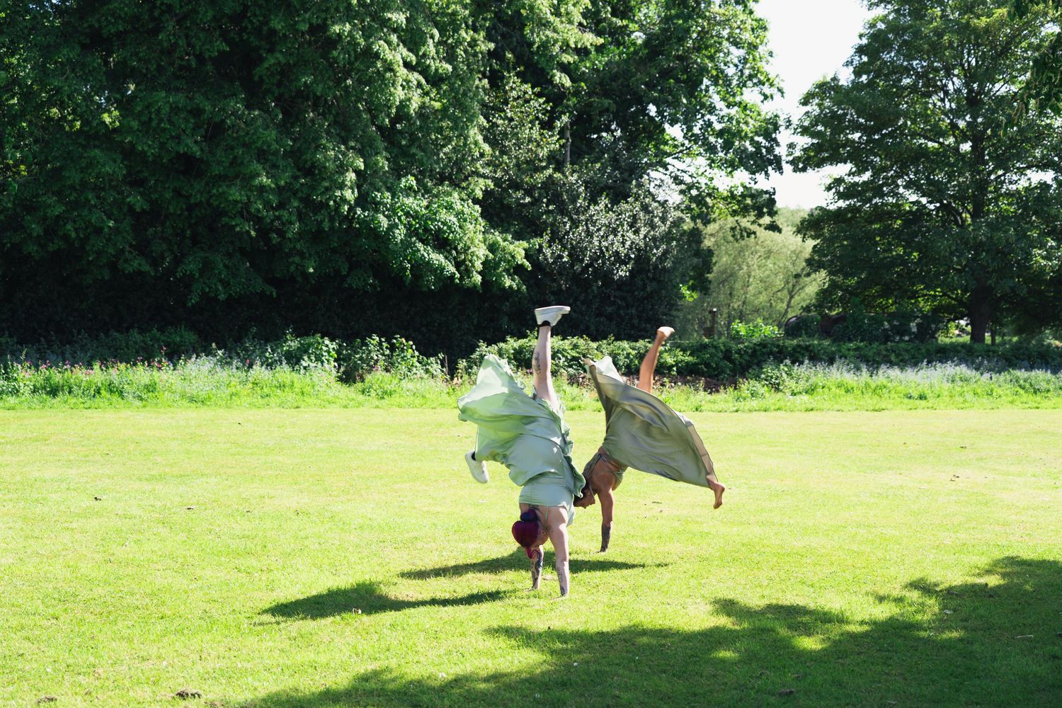 Wedding guest performs a cartwheel in a sunny green park during outdoor wedding celebration.