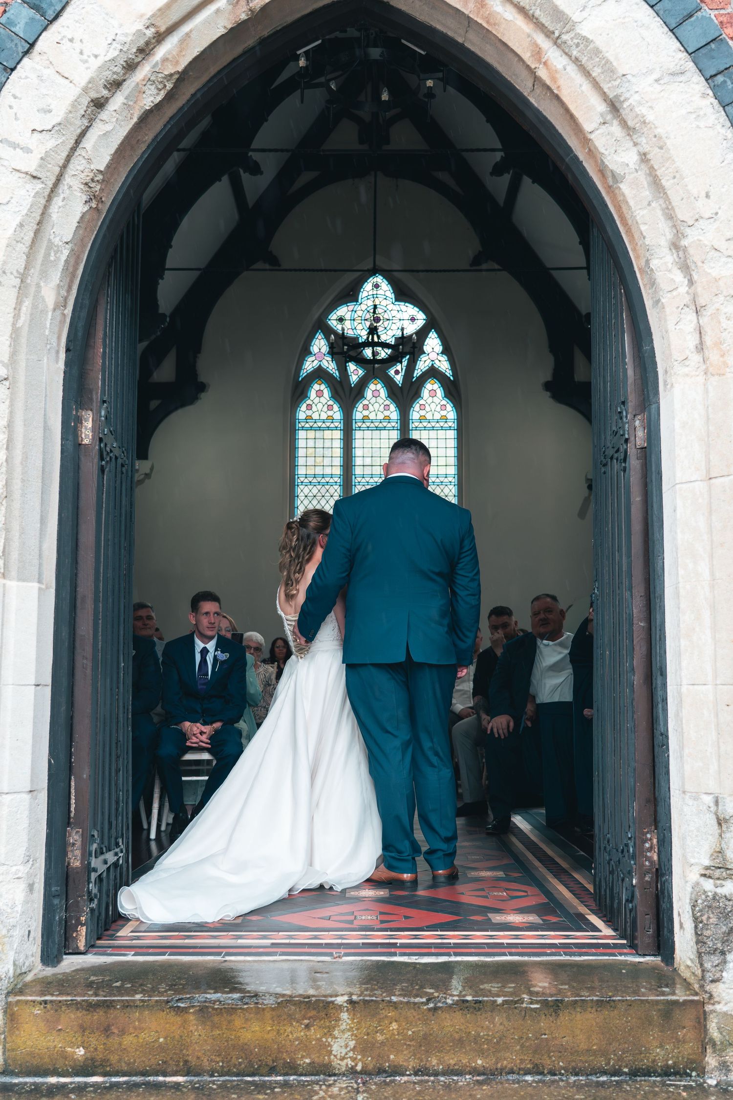 Bride and groom walking down the aisle viewed from behind through a church archway.