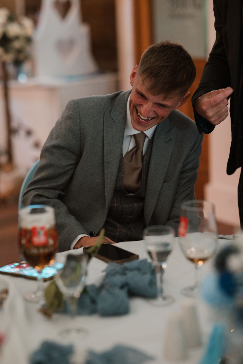 Wortley Hall - A person in a gray suit jacket smiles while looking down at a table with glasses and place settings.