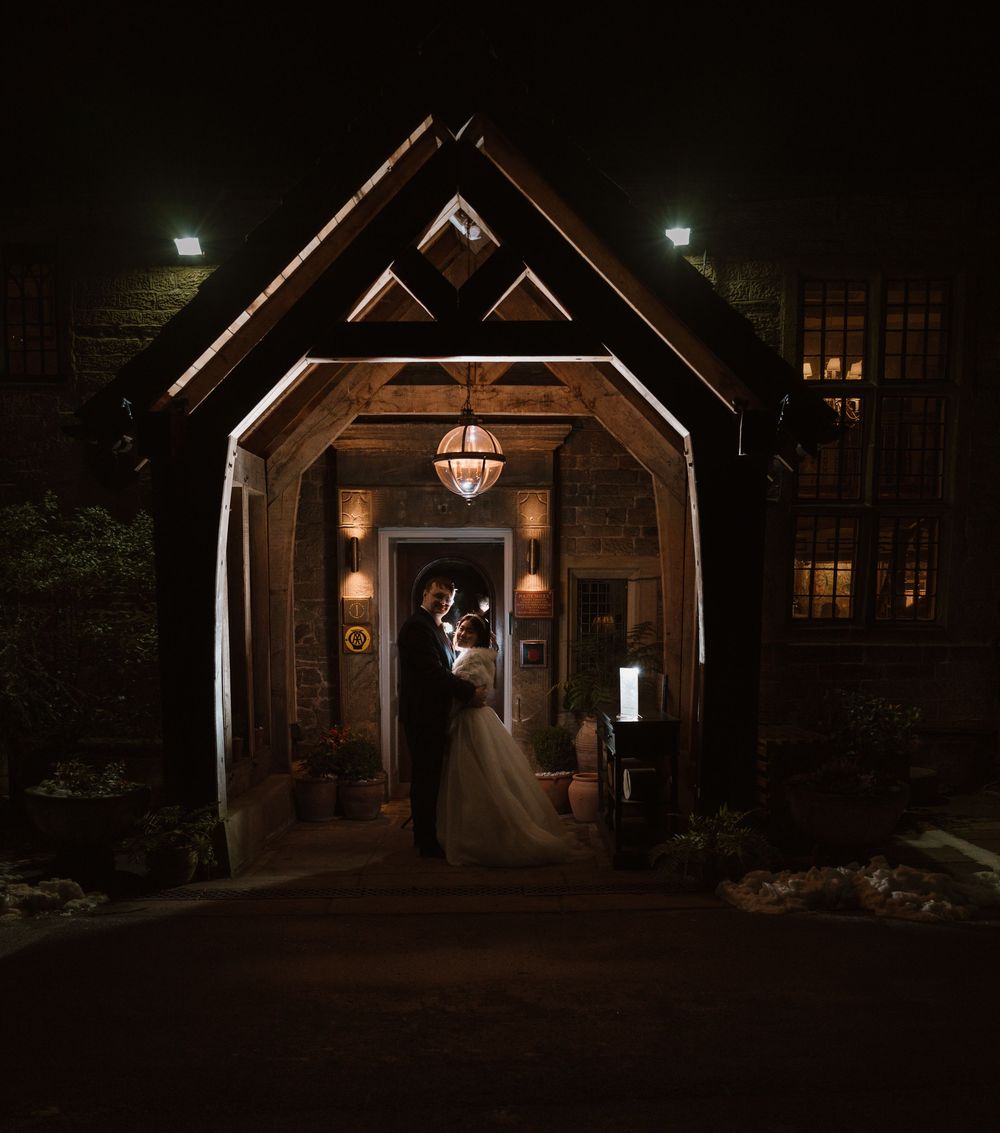 Whitely Hall - A romantic silhouette of a couple in formal attire standing under illuminated wooden beams at a rustic wedding venue.