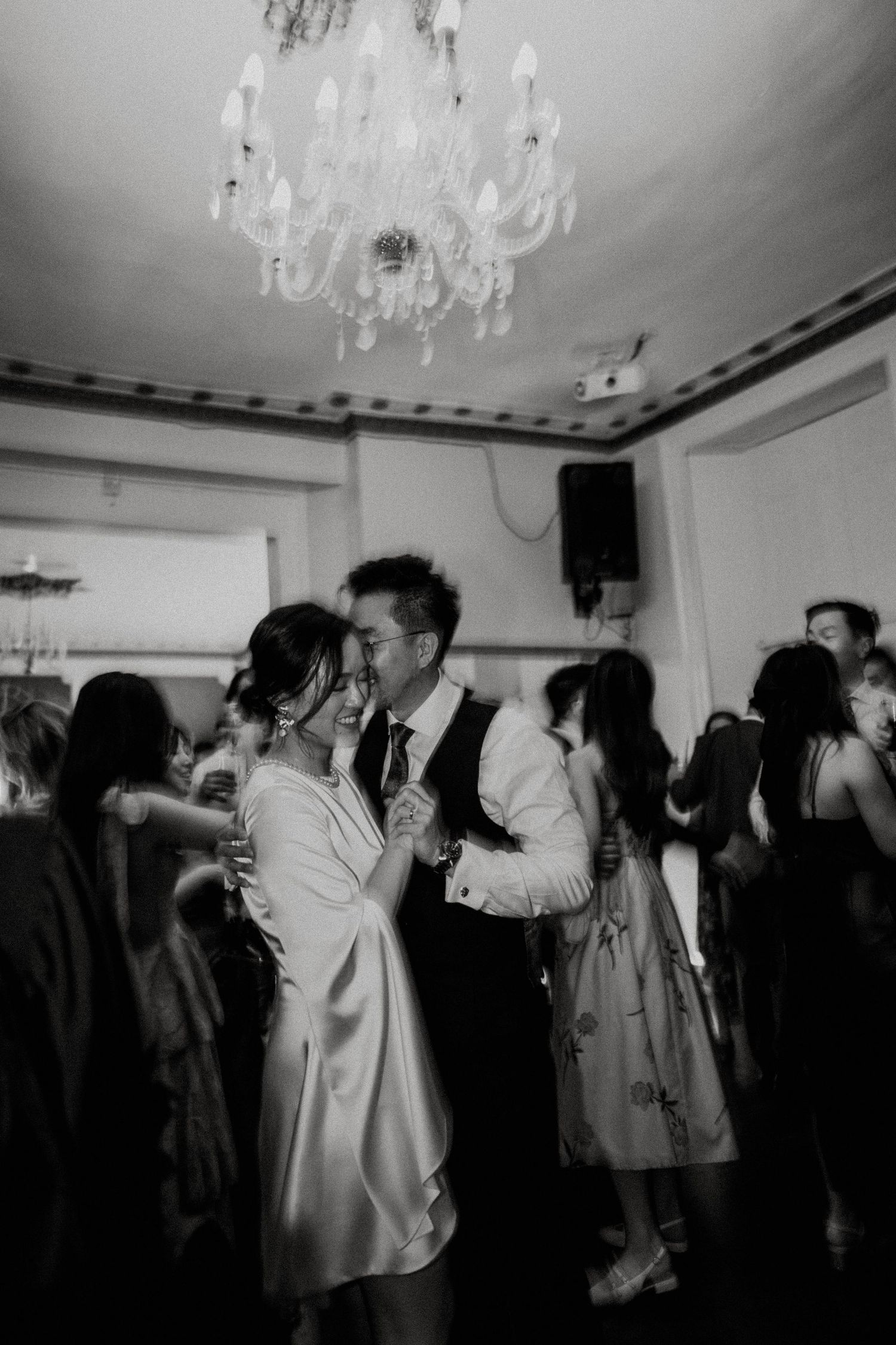 Black and white photos show people dancing and drinking at a party under elegant crystal chandeliers at Gosfield hall