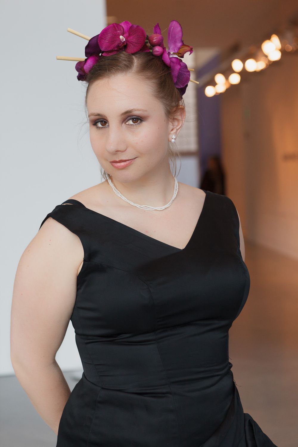 Elegant formal attire with purple orchid crown and pearl necklace in an indoor setting.