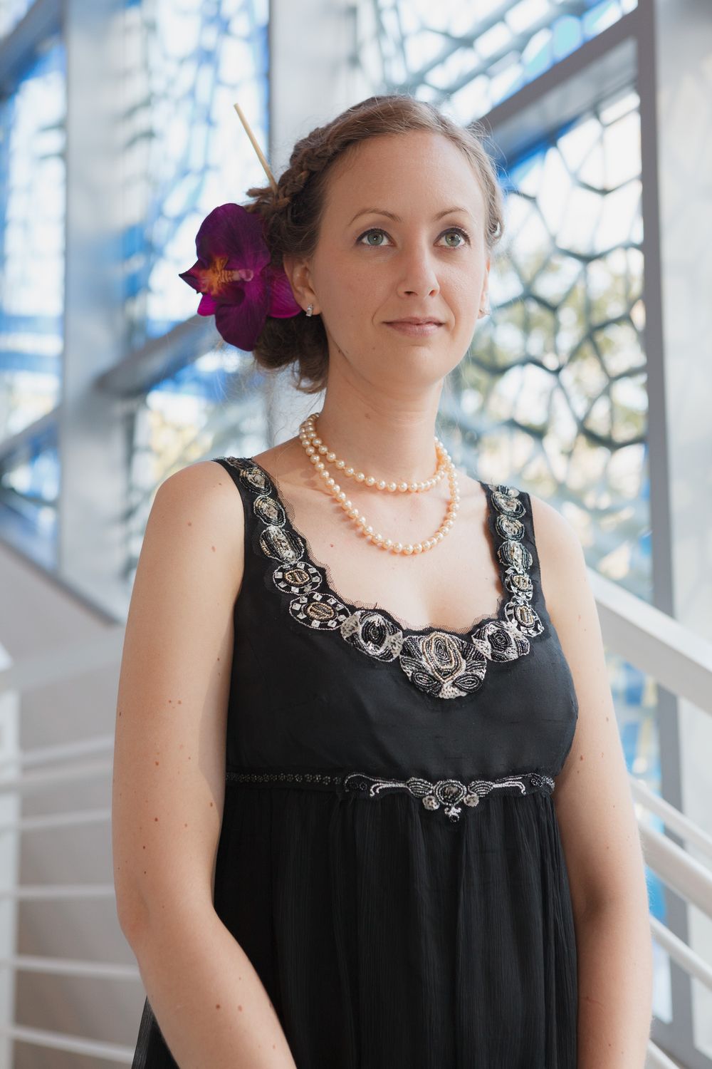 Formal black dress adorned with pearl necklace and purple orchid hair accessory.